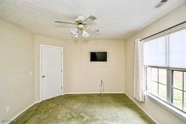 Carpeted empty room with ceiling fan and a textured ceiling