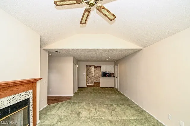 Unfurnished living room featuring carpet floors, ceiling fan, a tiled fireplace, a textured ceiling, and vaulted ceiling
