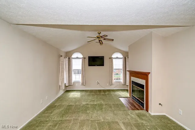 Unfurnished living room with carpet, a tile fireplace, a ceiling fan, lofted ceiling, and a textured ceiling