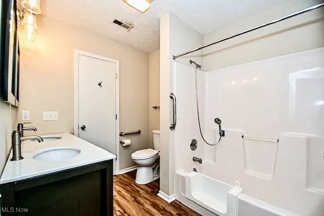 Bathroom featuring wood finished floors, shower / tub combination, double vanity, and a textured ceiling