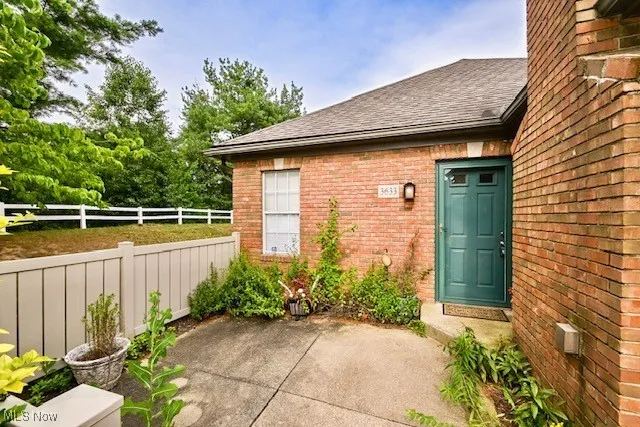View of exterior entry with brick siding, roof with shingles, and a patio