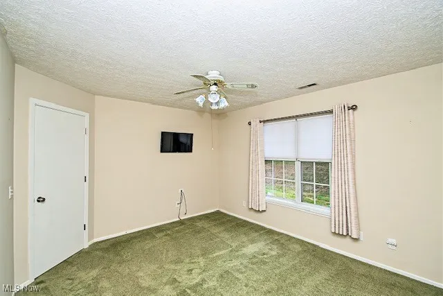Unfurnished room featuring carpet, a ceiling fan, and a textured ceiling