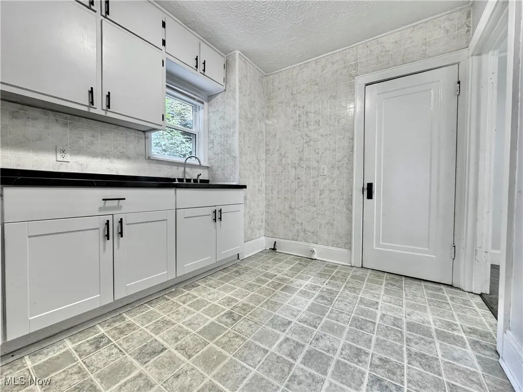 Kitchen with a textured ceiling, dark countertops, and white cabinets
