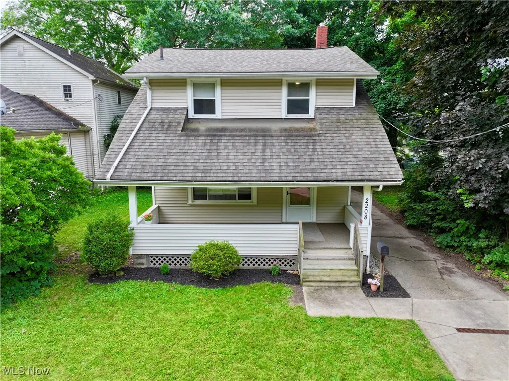 View of front of house featuring covered porch, a chimney, roof with shingles, and a front lawn