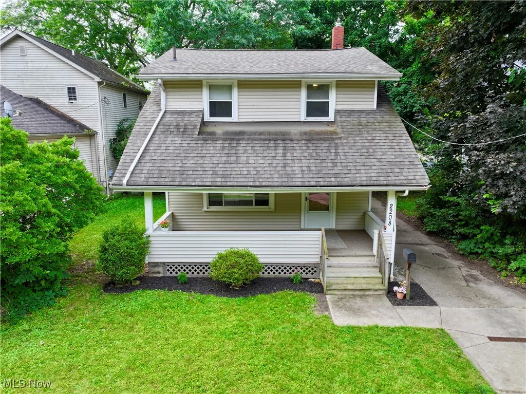 View of front facade featuring covered porch, a chimney, roof with shingles, and a front yard