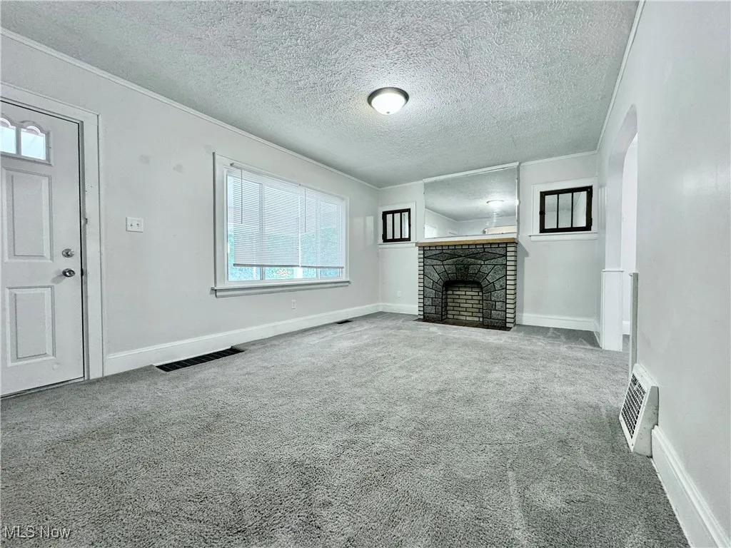 Unfurnished living room with carpet, a fireplace, arched walkways, and a textured ceiling