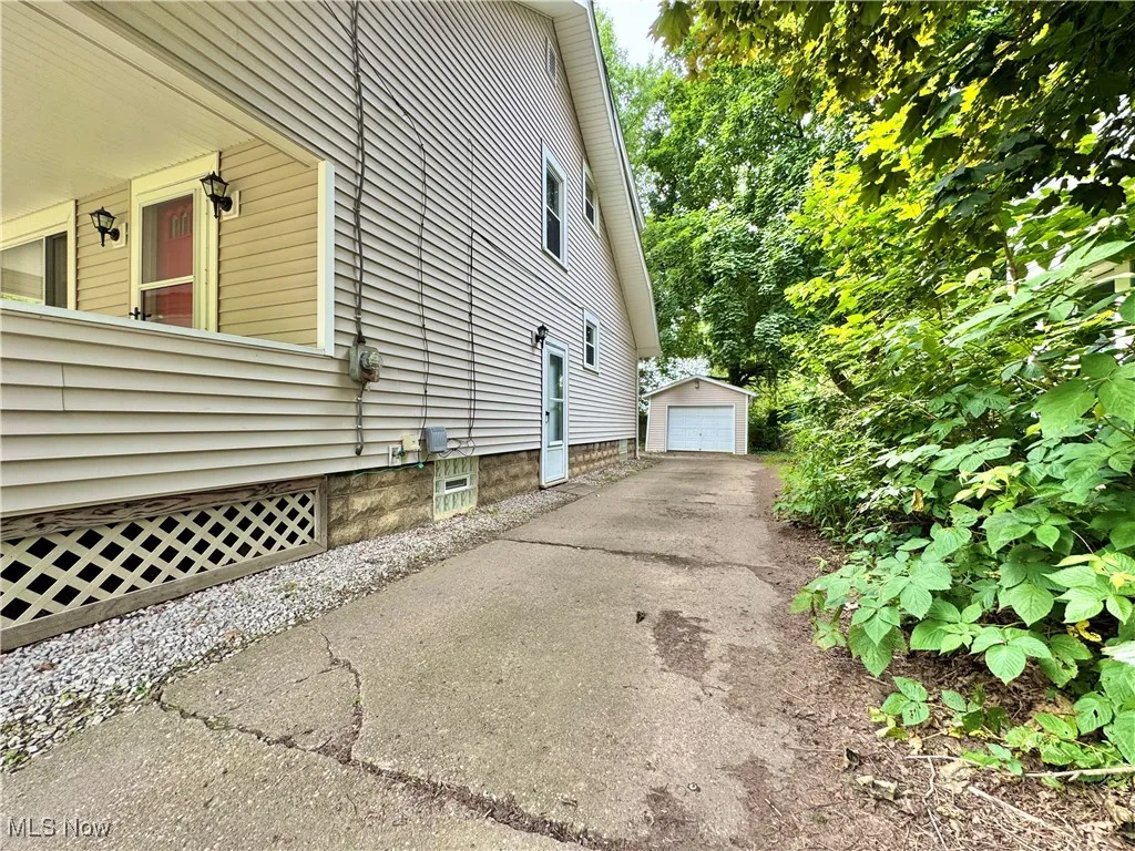 View of property exterior with driveway, an outdoor structure, and a detached garage