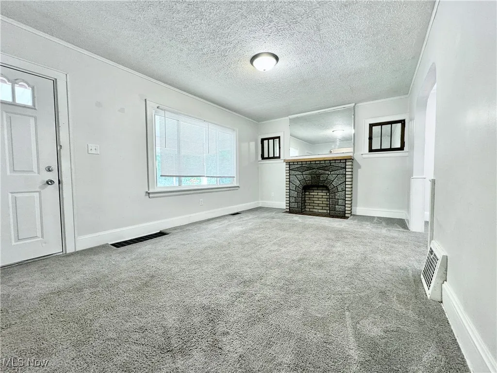 Unfurnished living room with carpet flooring, a fireplace, arched walkways, a textured ceiling, and ornamental molding