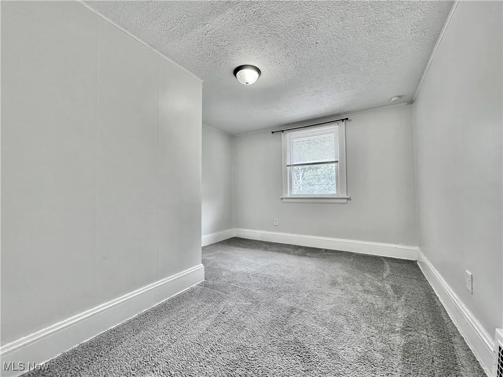 Carpeted spare room featuring a textured ceiling and baseboards