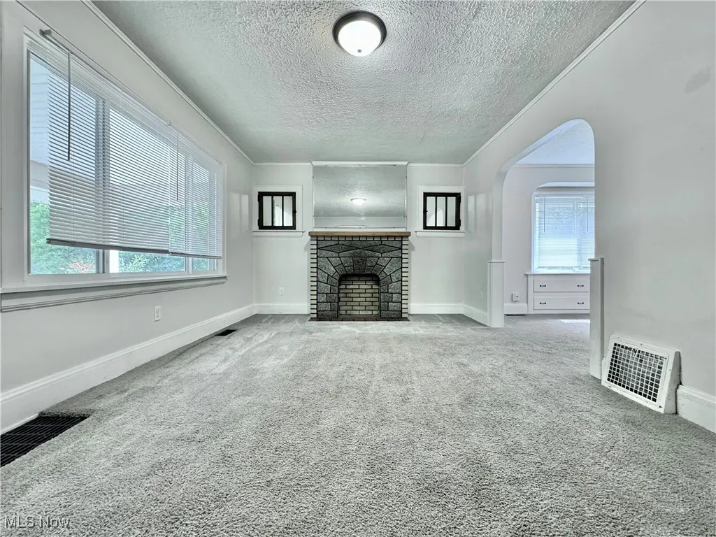 Unfurnished living room featuring carpet floors, a textured ceiling, a fireplace, arched walkways, and crown molding