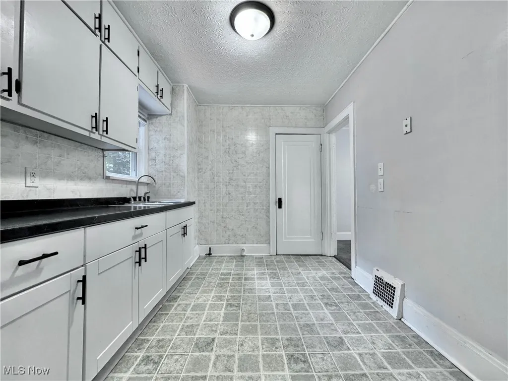 Kitchen featuring a textured ceiling, white cabinetry, and dark countertops
