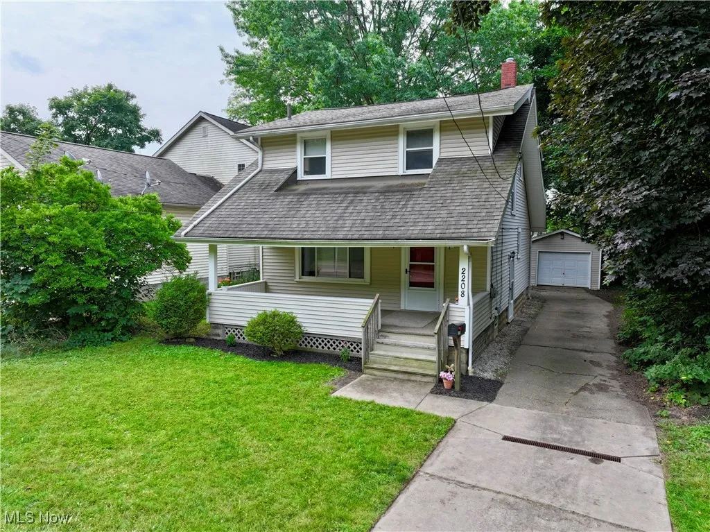 View of front facade featuring concrete driveway, a chimney, an outdoor structure, covered porch, and a garage