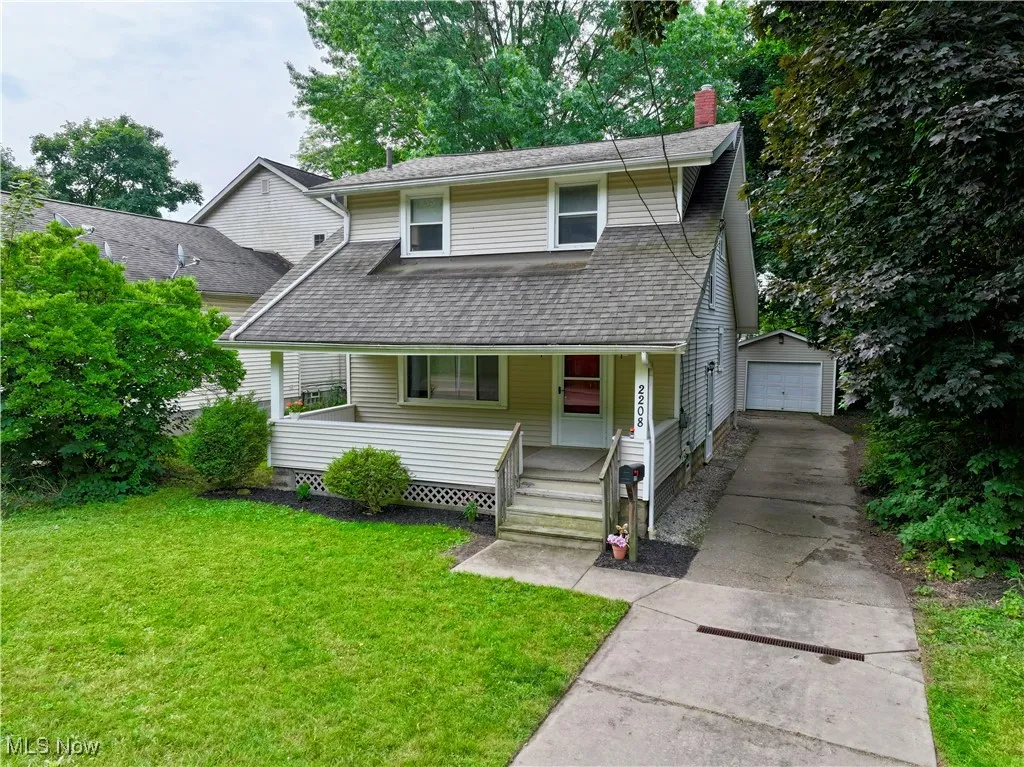 View of front of house with driveway, a chimney, an outdoor structure, covered porch, and roof with shingles