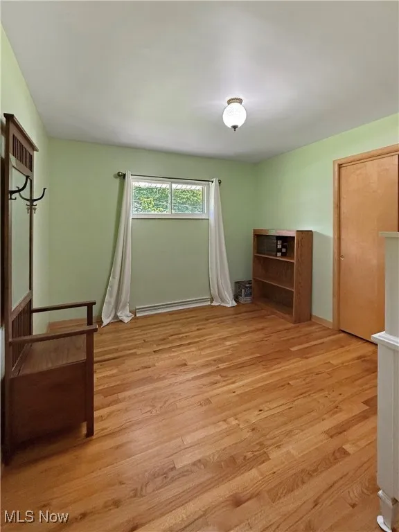 Unfurnished bedroom with a baseboard heating unit and light wood-style floors