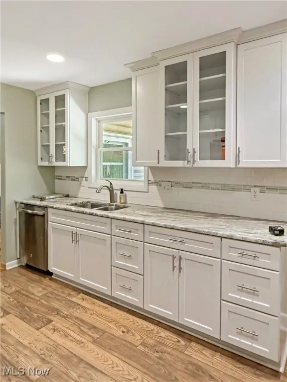 Kitchen with dishwasher, light wood finished floors, backsplash, glass insert cabinets, and white cabinetry