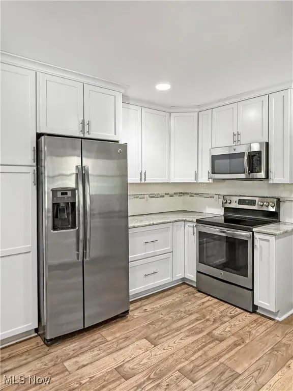 Kitchen with appliances with stainless steel finishes, white cabinets, light wood-style flooring, and recessed lighting