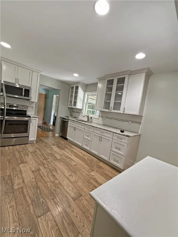 Kitchen featuring appliances with stainless steel finishes, light wood-style flooring, light countertops, recessed lighting, and glass insert cabinets