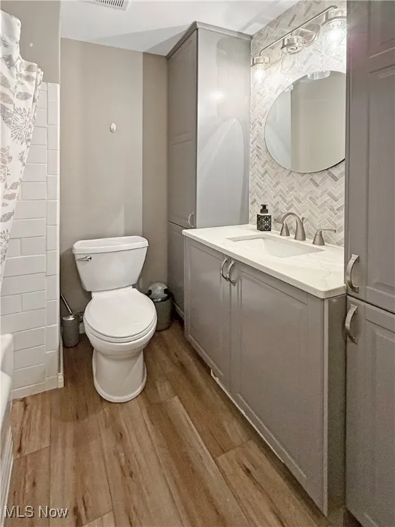Full bath with wood finished floors, vanity, and decorative backsplash