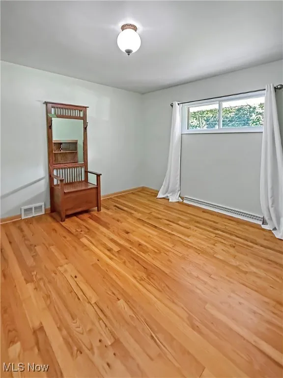 Unfurnished room featuring baseboard heating and light wood finished floors