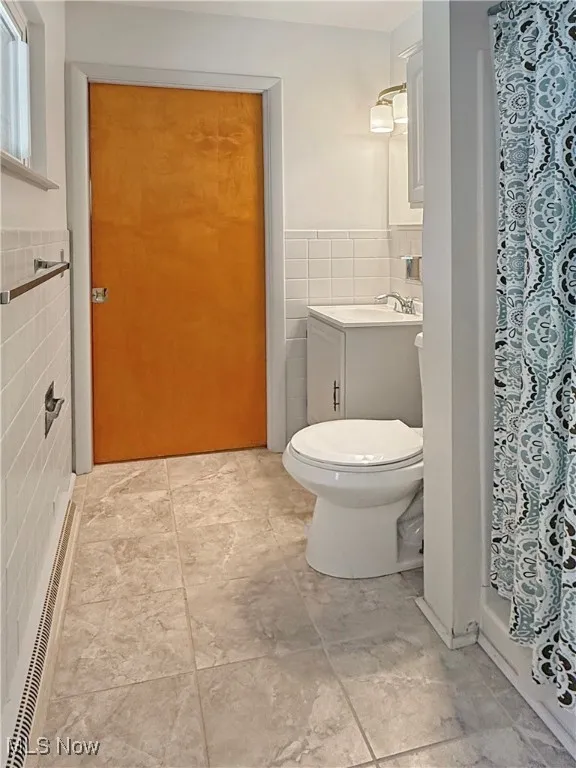 Bathroom with tile walls, vanity, a shower with shower curtain, and a wainscoted wall