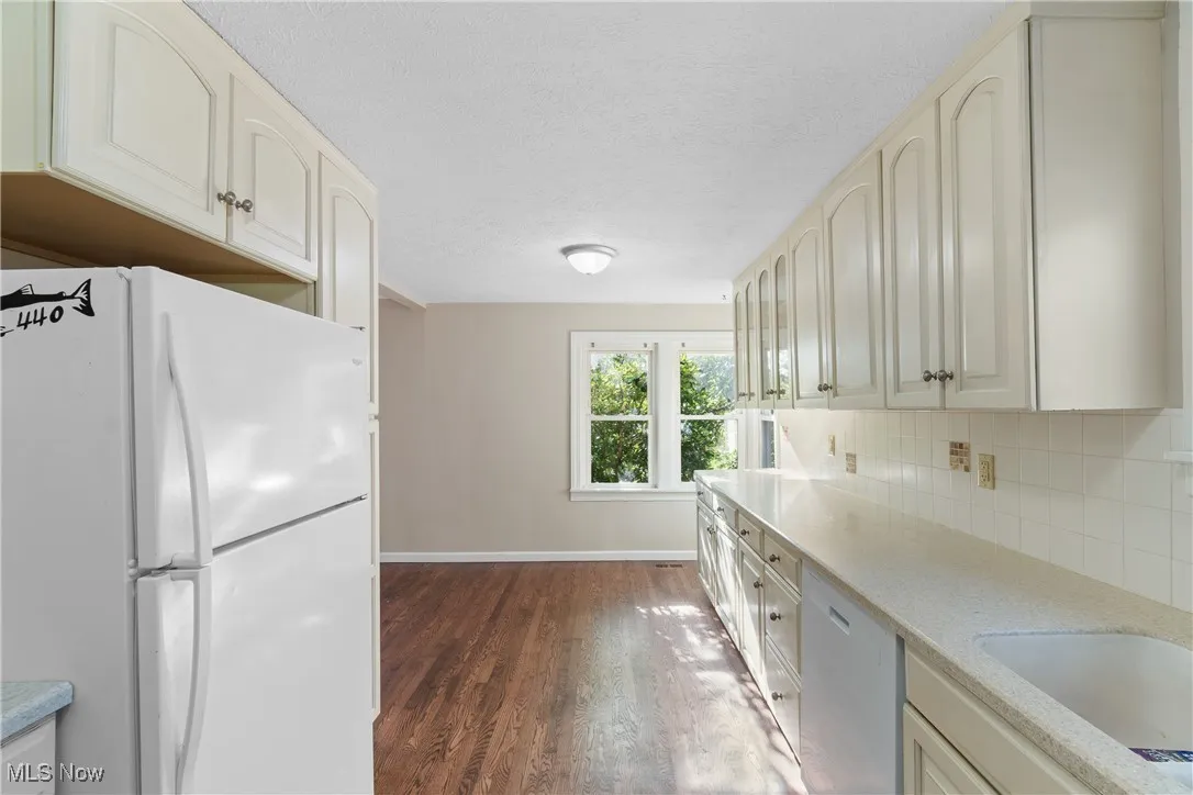 Kitchen featuring freestanding refrigerator, dishwasher, dark wood-style floors, tasteful backsplash, and light countertops