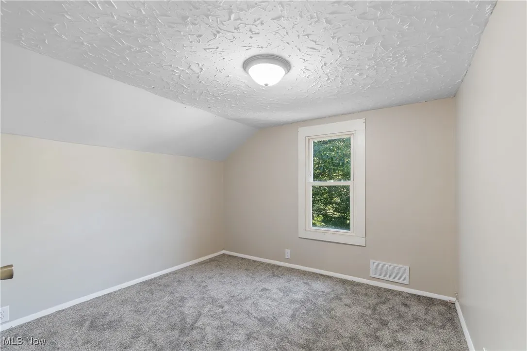 Bedroom featuring carpet floors, vaulted ceiling, and a textured ceiling