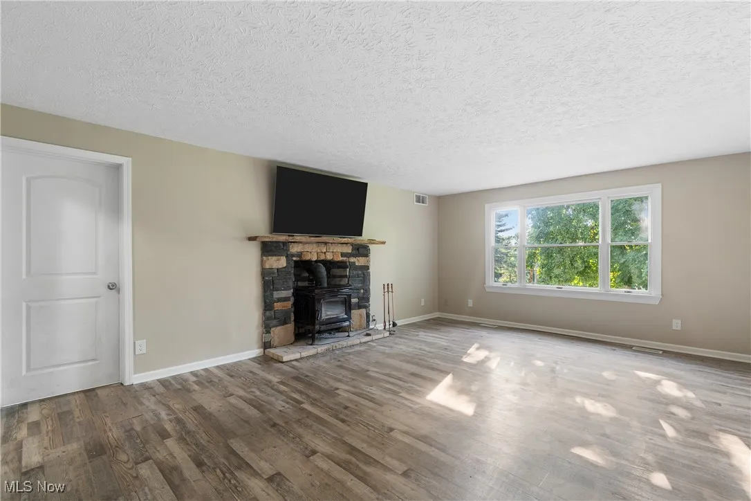 Unfurnished living room with wood finished floors, a wood stove, and a textured ceiling