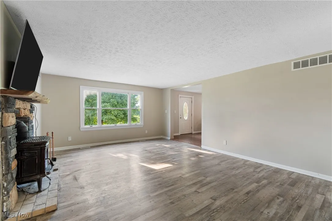 Unfurnished living room featuring wood finished floors, a wood stove, and a textured ceiling