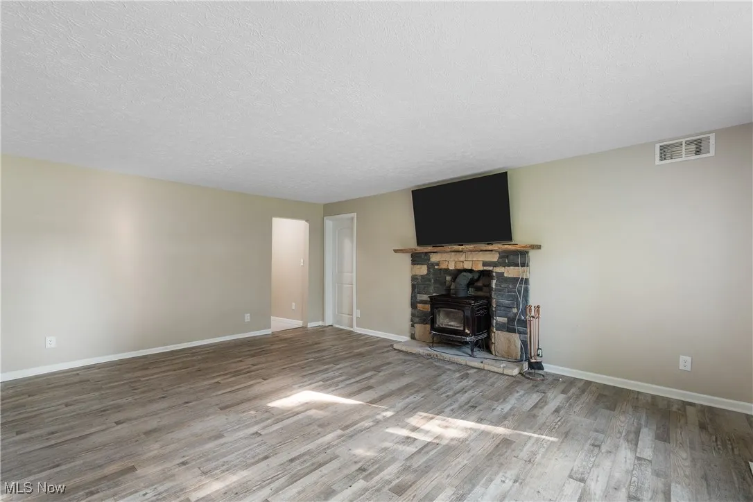 Unfurnished living room with a wood stove, wood finished floors, and a textured ceiling