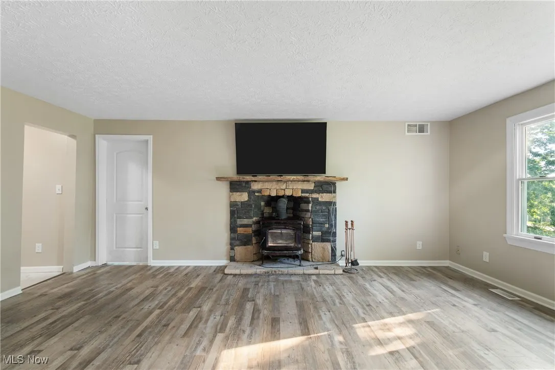 Unfurnished living room featuring a textured ceiling, wood finished floors, and a wood stove