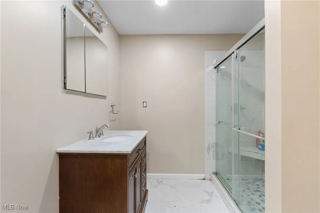 Full bathroom on the first floor featuring vanity, a marble finish shower, and marble finish flooring
