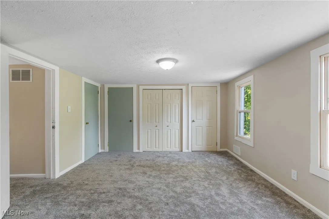 Unfurnished bedroom featuring multiple closets, a textured ceiling, and carpet flooring