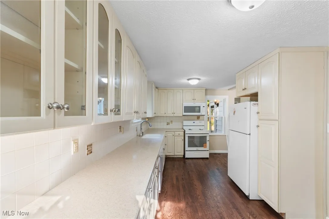 Kitchen featuring white appliances, cream cabinetry, light countertops, glass insert cabinets, and a textured ceiling