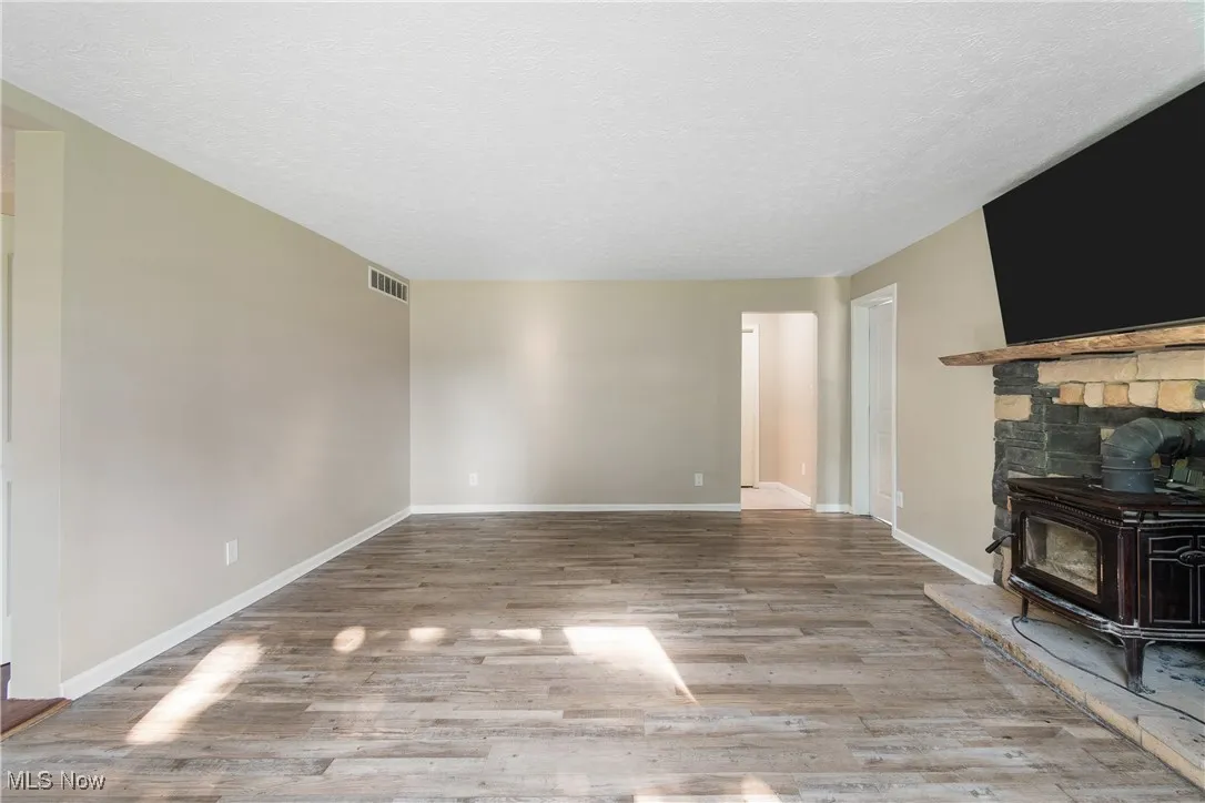 Unfurnished living room featuring a wood stove, wood finished floors, and a textured ceiling