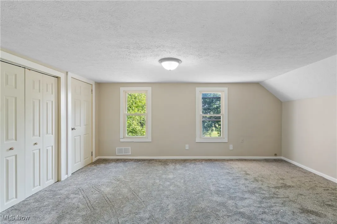 second floor bedroom with two closets, carpet flooring, multiple windows, and a textured ceiling