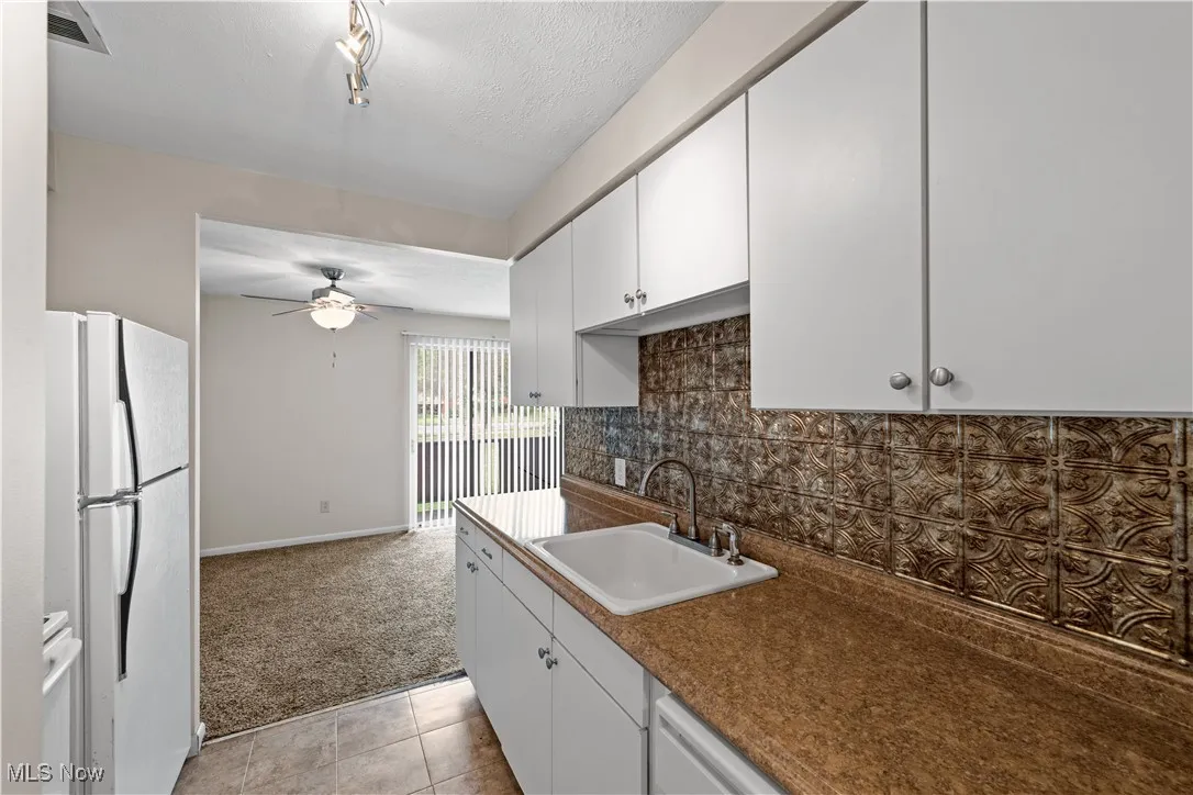 Kitchen featuring freestanding refrigerator, white cabinetry, and decorative backsplash