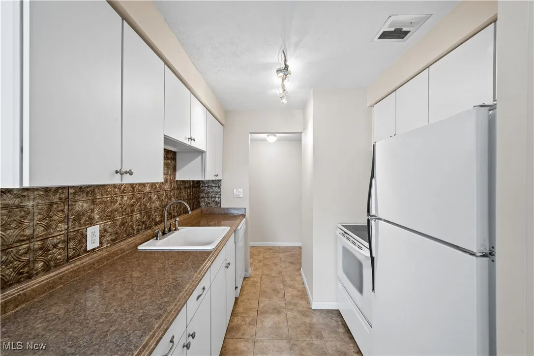 Kitchen featuring white appliances, backsplash, dark countertops, white cabinetry, and light tile patterned floors