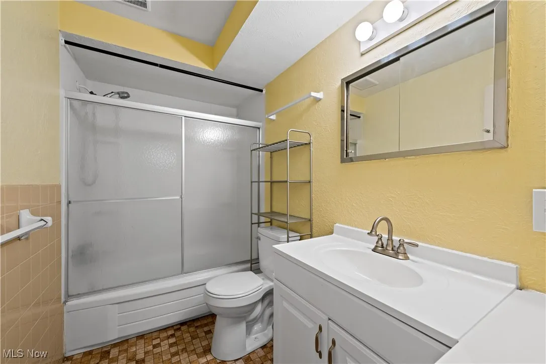 Full bathroom featuring vanity, shower / bath combination with glass door, and a textured wall