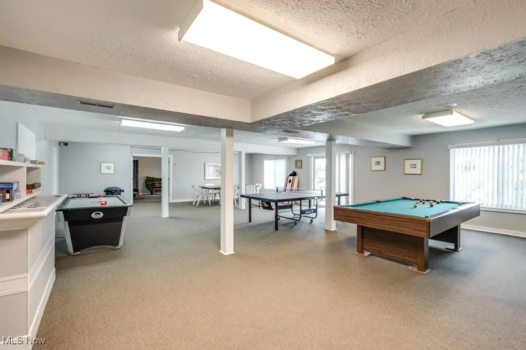 Rec room at club house with pool table, a textured ceiling, plenty of natural light, and light carpet