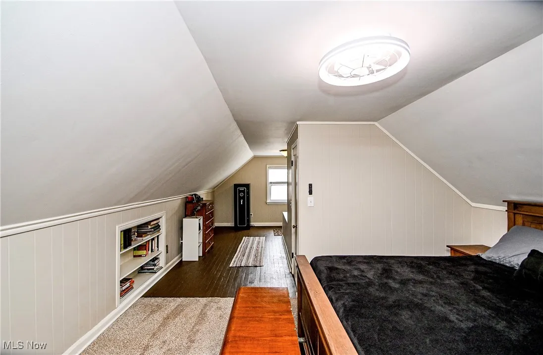 Bedroom featuring dark wood finished floors, vaulted ceiling, and wooden walls