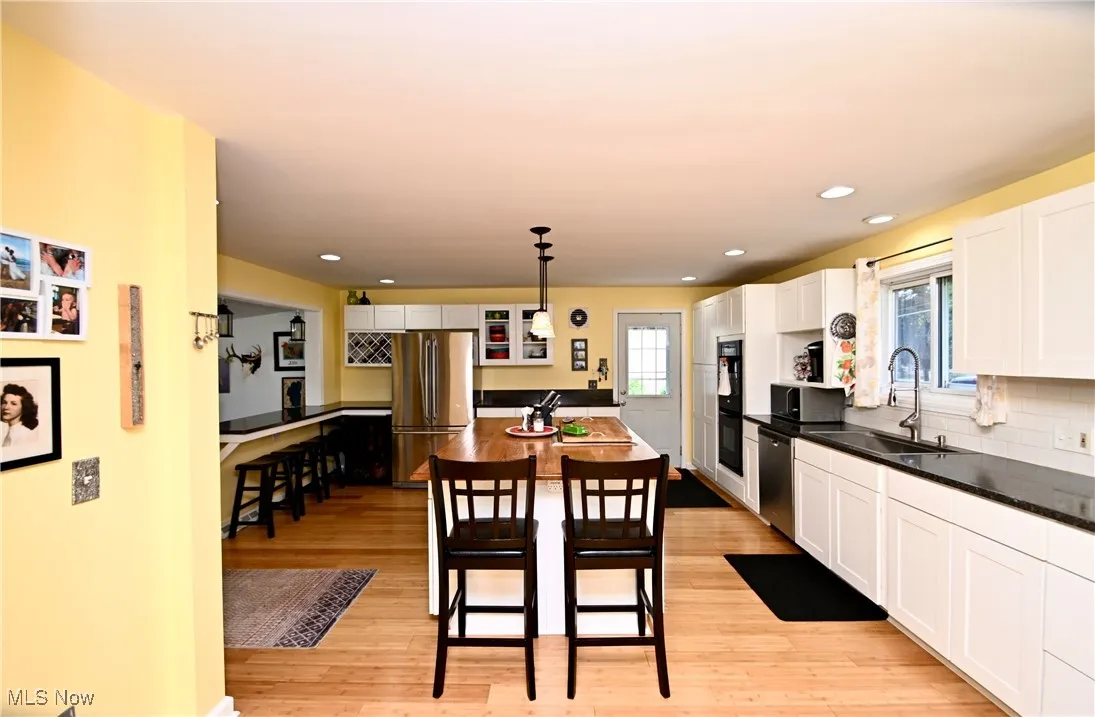 Kitchen with stainless steel appliances, light wood-style flooring, white cabinets, dark countertops, and decorative backsplash