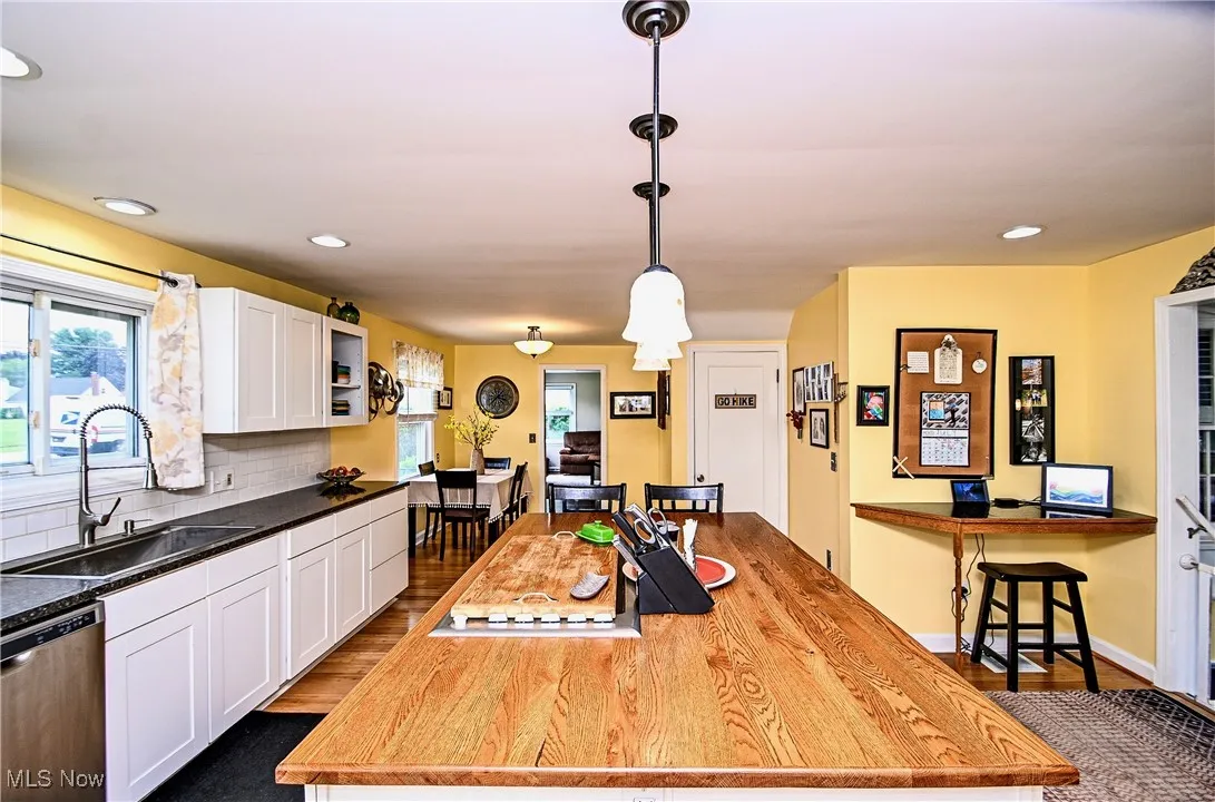 Kitchen featuring stainless steel dishwasher, white cabinetry, wood-style floors, backsplash, and hanging light fixtures