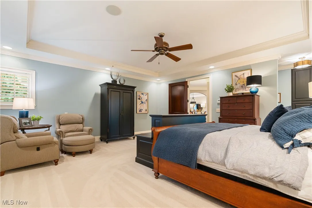 Master suite with a tray ceiling, fan, and corner sitting area.