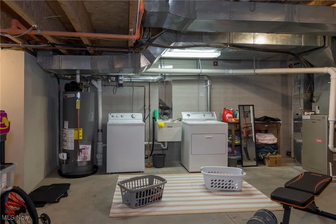 Unfinished below grade area with gas water heater, washing machine and clothes dryer, and heating unit