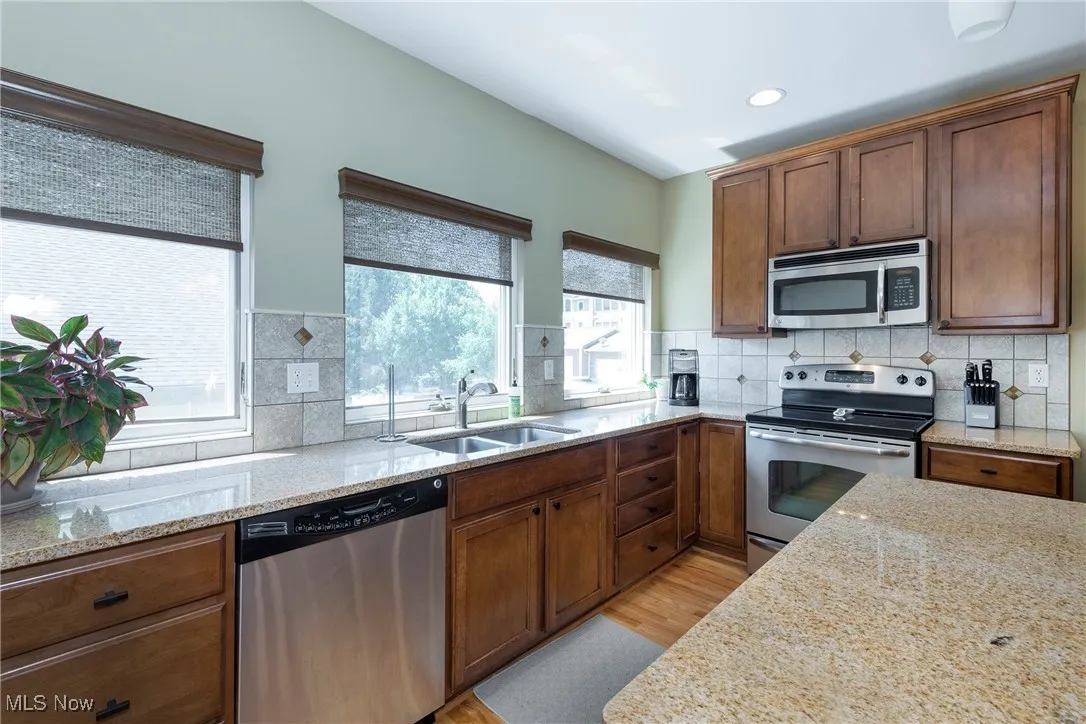 Kitchen featuring appliances with stainless steel finishes, light wood-style flooring, light stone counters, tasteful backsplash, and recessed lighting