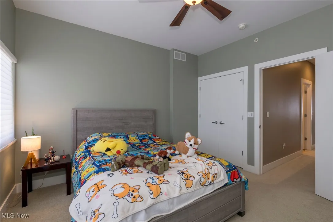 Bedroom with light colored carpet, a ceiling fan, and a closet