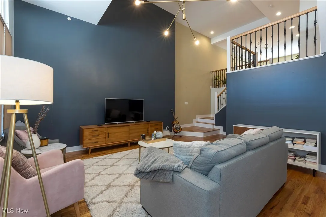 Living room featuring a high ceiling, stairs, wood finished floors, and recessed lighting