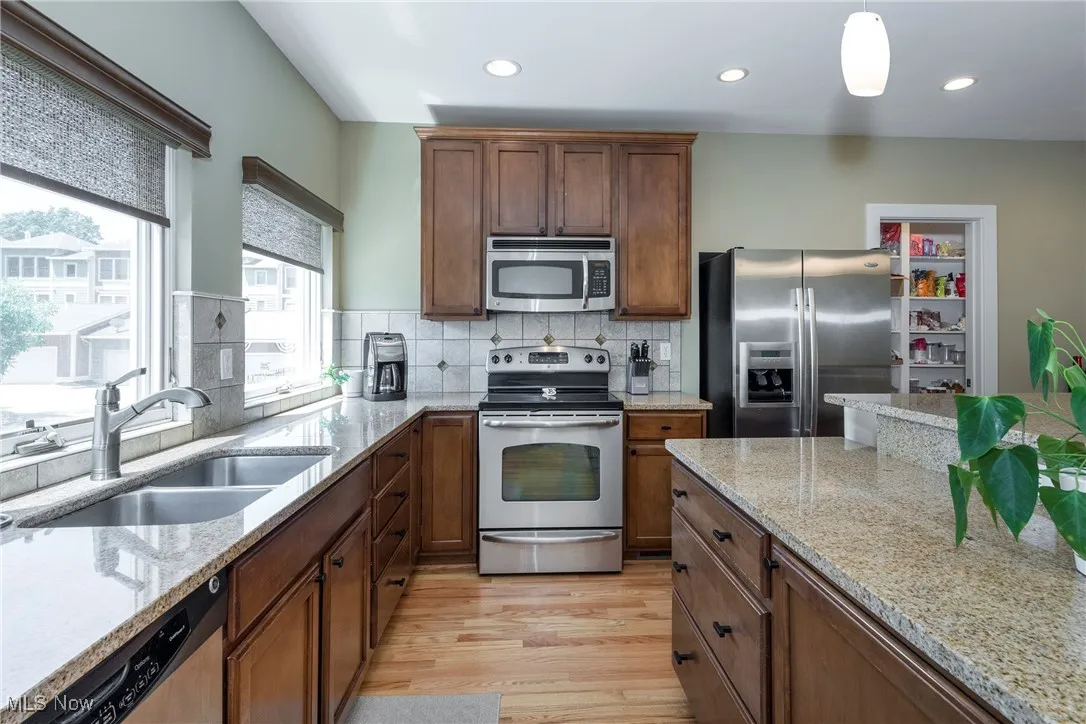 Kitchen with appliances with stainless steel finishes, light wood-style floors, decorative backsplash, brown cabinets, and light stone counters