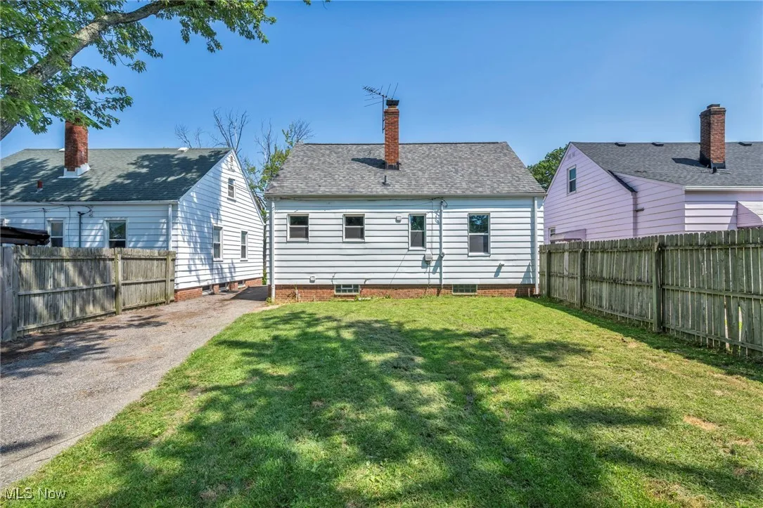 Back of property with a fenced backyard, a chimney, and asphalt driveway