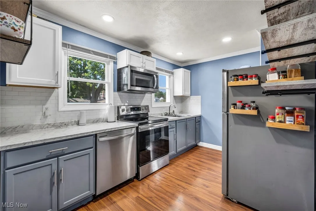 Kitchen with stainless steel appliances, crown molding, open shelves, backsplash, and light wood-style floors